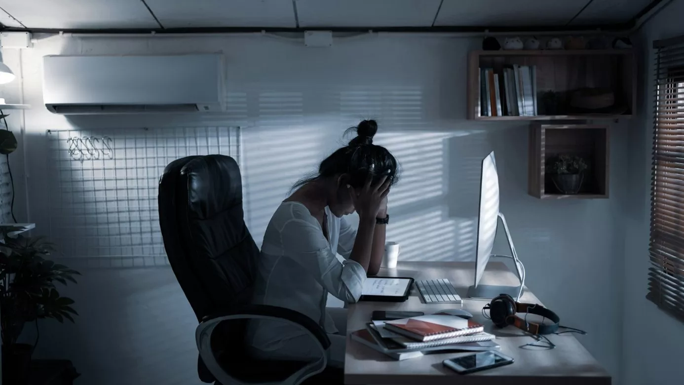 Frau mit Hände am Kopf sitzt im Dunkeln vor ihrem Laptop