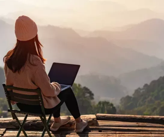 Studentin arbeitet online mit Laptop und genießt die schöne Landschaft mit Blick auf die Berge bei Sonnenaufgang