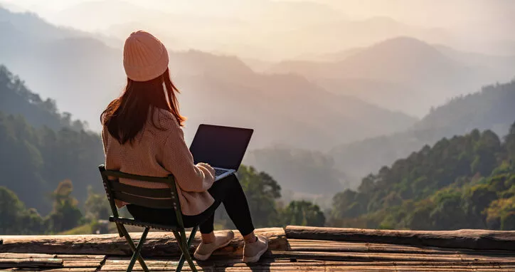 Studentin arbeitet online mit Laptop und genießt die schöne Landschaft mit Blick auf die Berge bei Sonnenaufgang