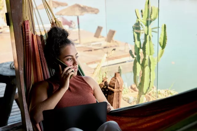 Frau liegt in der Hängematte mit Strand im Hintergrund und telefoniert