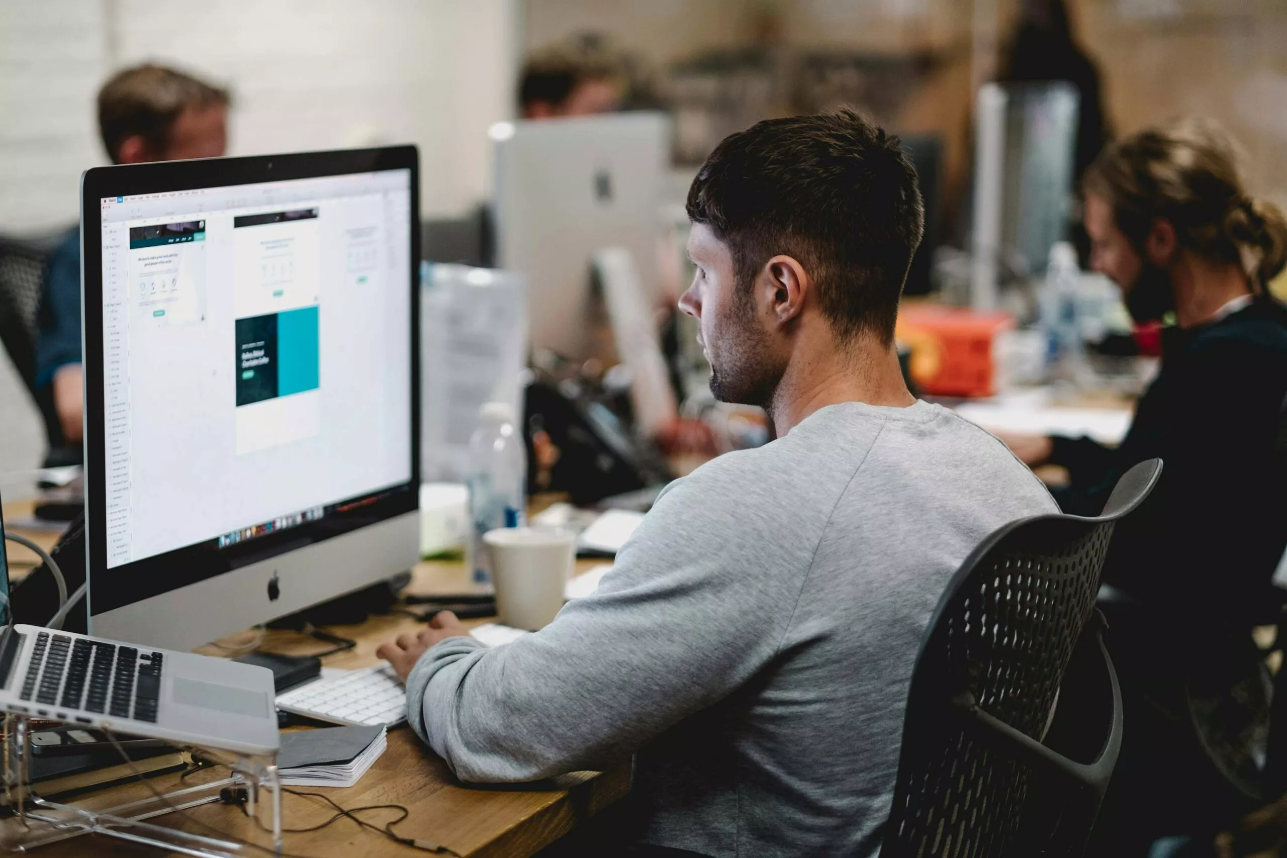 Student sitzt am Tisch vor einem iMac und schaut auf den Bildschirm