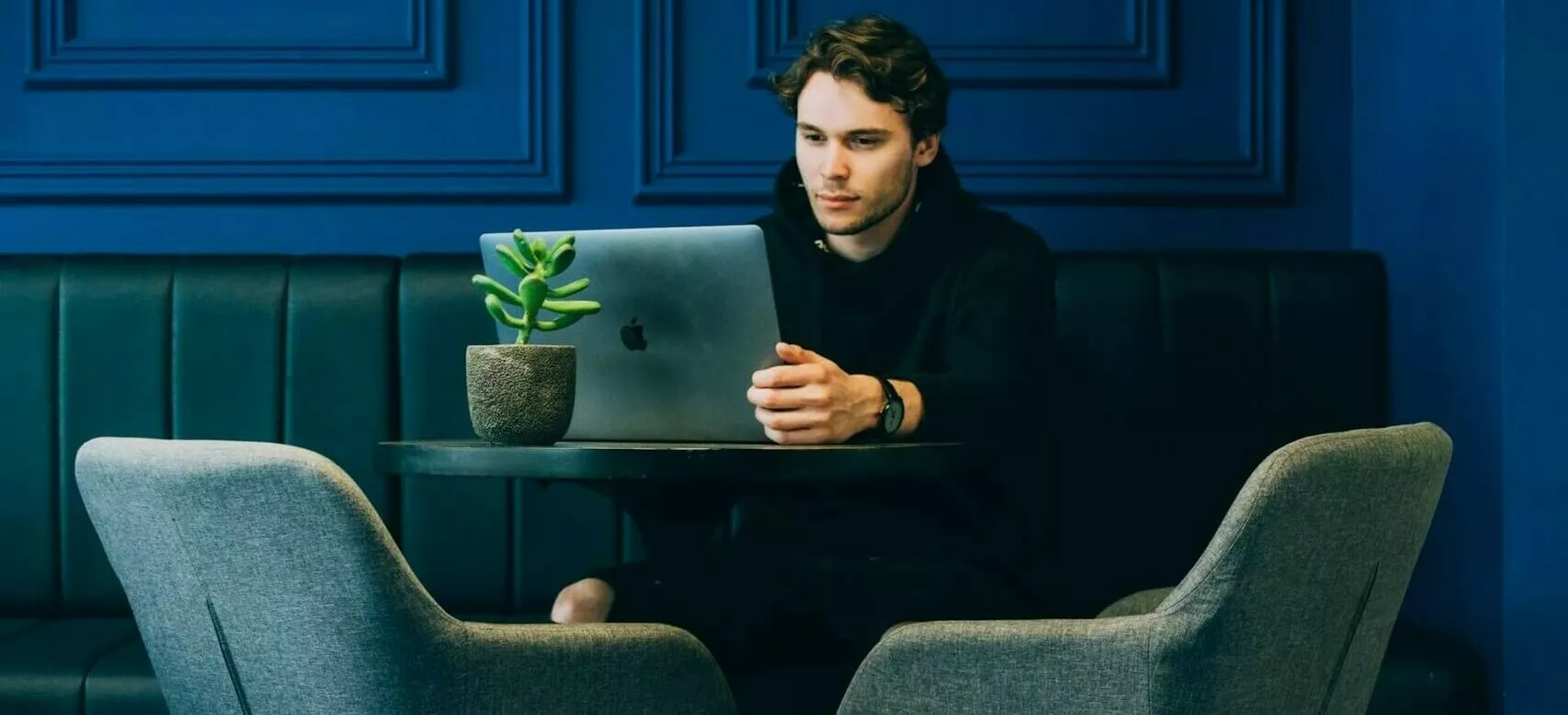 Student sitzt in einem blauen Zimmer vor seinem Laptop