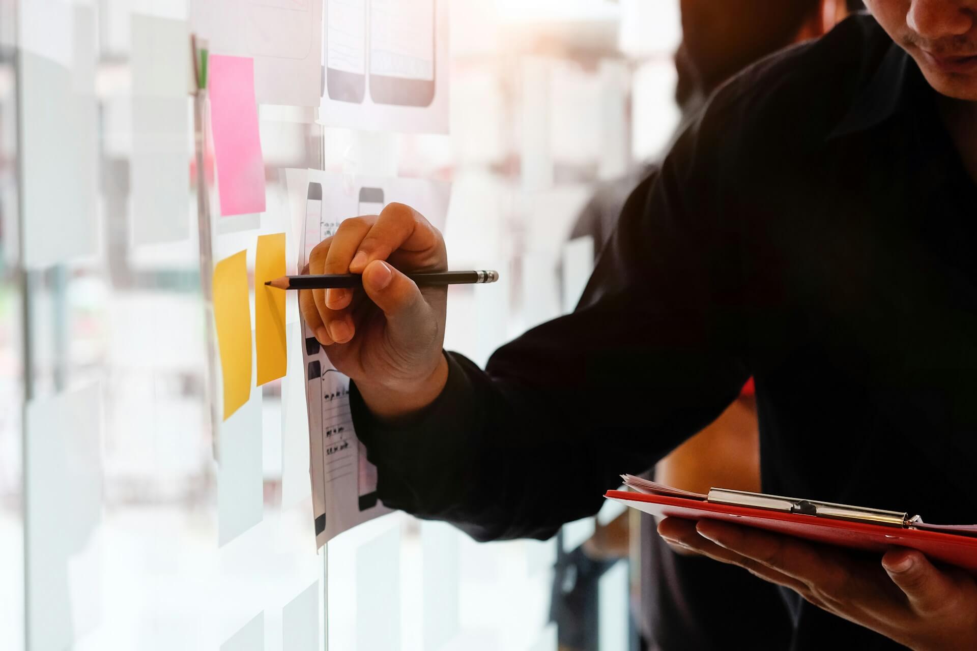 Ein Mann mit Klemmbrett und Stift in der Hand beschriftet einen Post-it